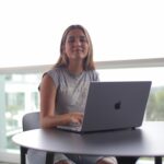 A young woman sits outdoors with a laptop, focused on online learning.